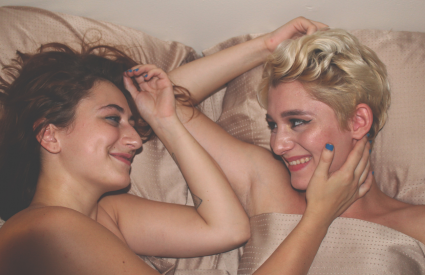 two women laying in bed gazing at each other
